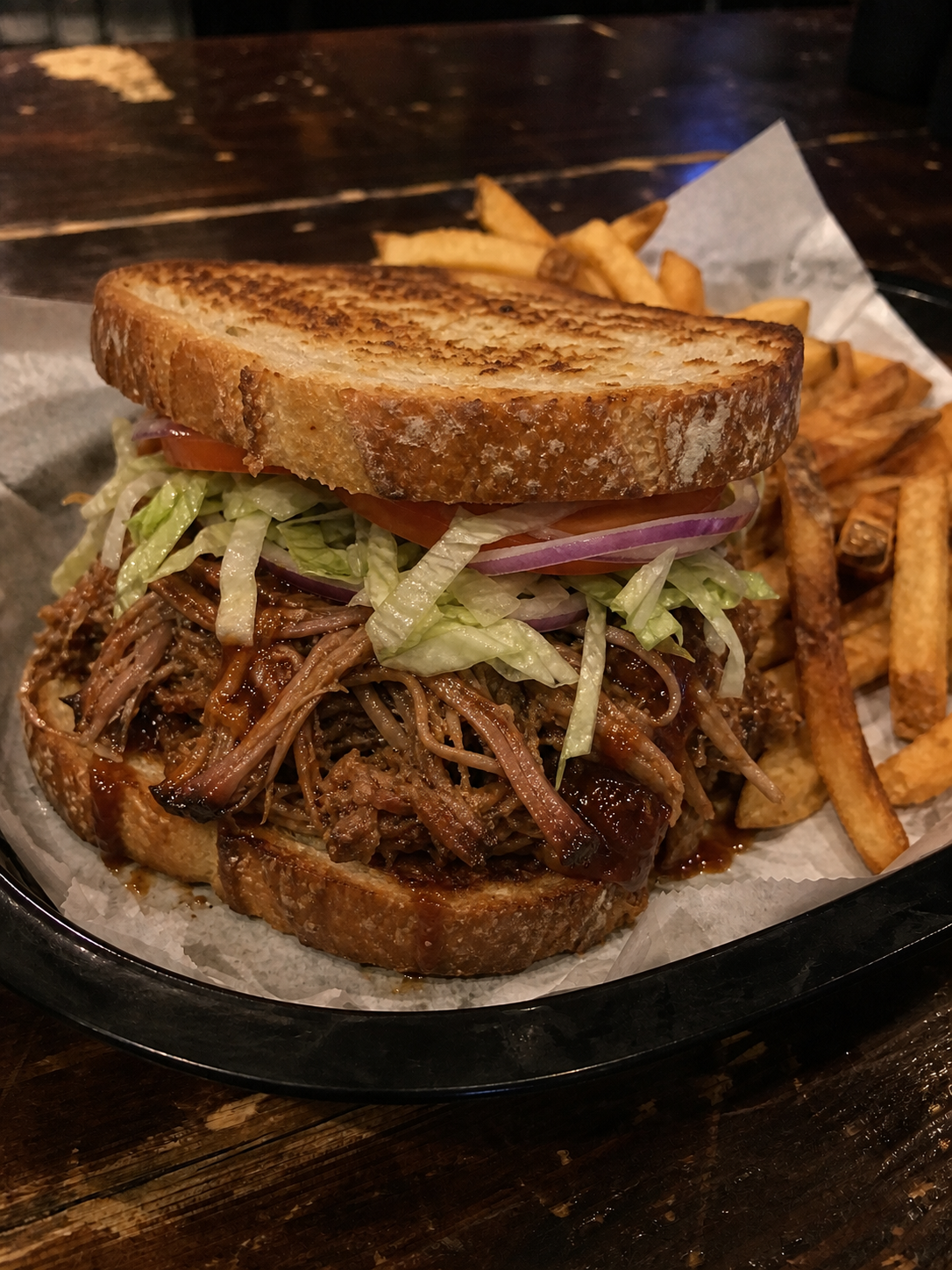 BBQ pulled pork sandwich on toasted sourdough with lettuce, onion, tomato and fries